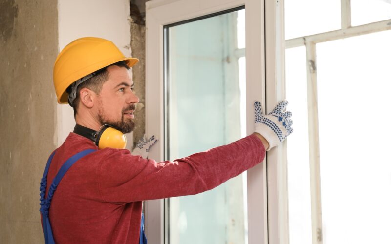 Worker in uniform installing plastic window indoors